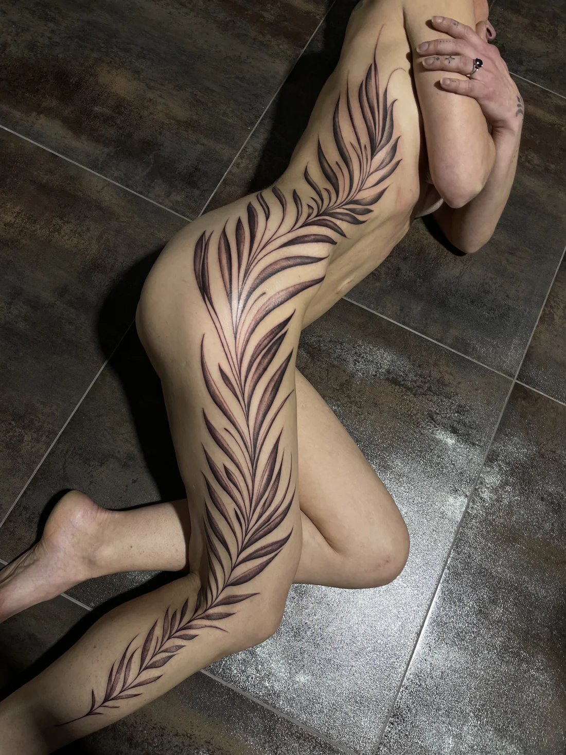 Grand tatouage de feuillage noir et gris suivant le flanc et la jambe, par Leali Tattoo